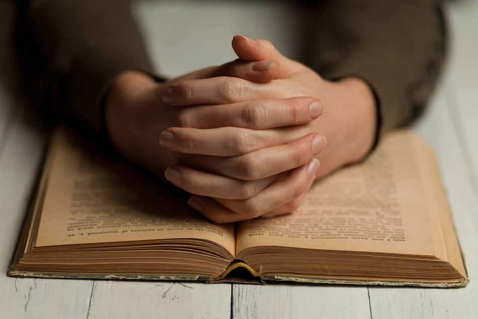 Open Bible with hands in prayer, illustrating a moment of contemplation and connection to faith.