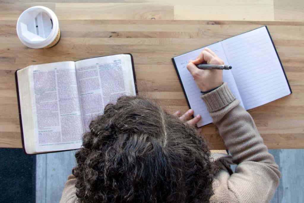 black woman sits and studying her bible with journal while drinking coffee